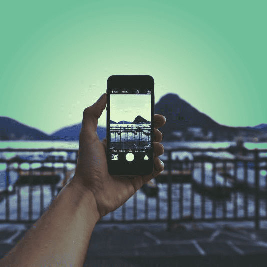 arm holding up a camera on smartphone taking picture of a mountain