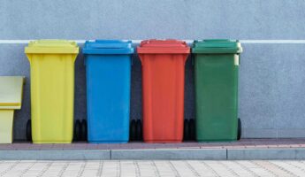 different coloured recycling bins lined up against wall