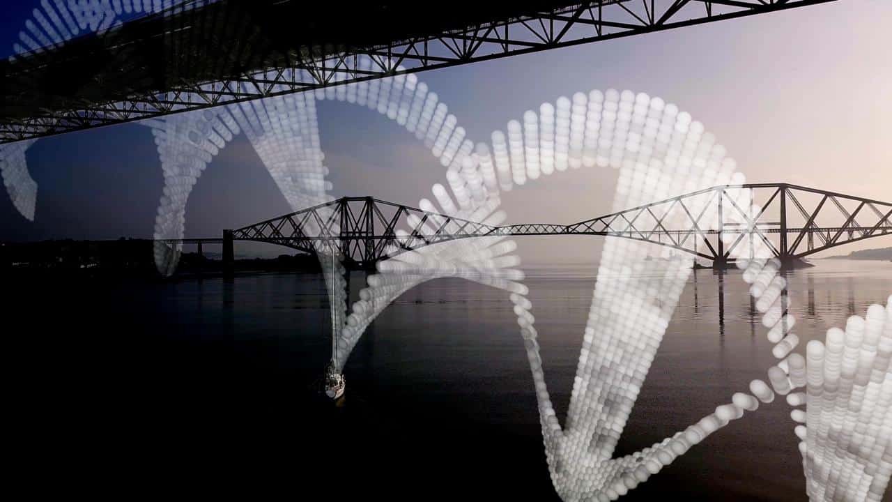 A suspension bridge spans across a calm river under a clear sky, with large white DNA helix structures superimposed over the scene. Another bridge is visible in the background, enhancing the architectural perspective.
