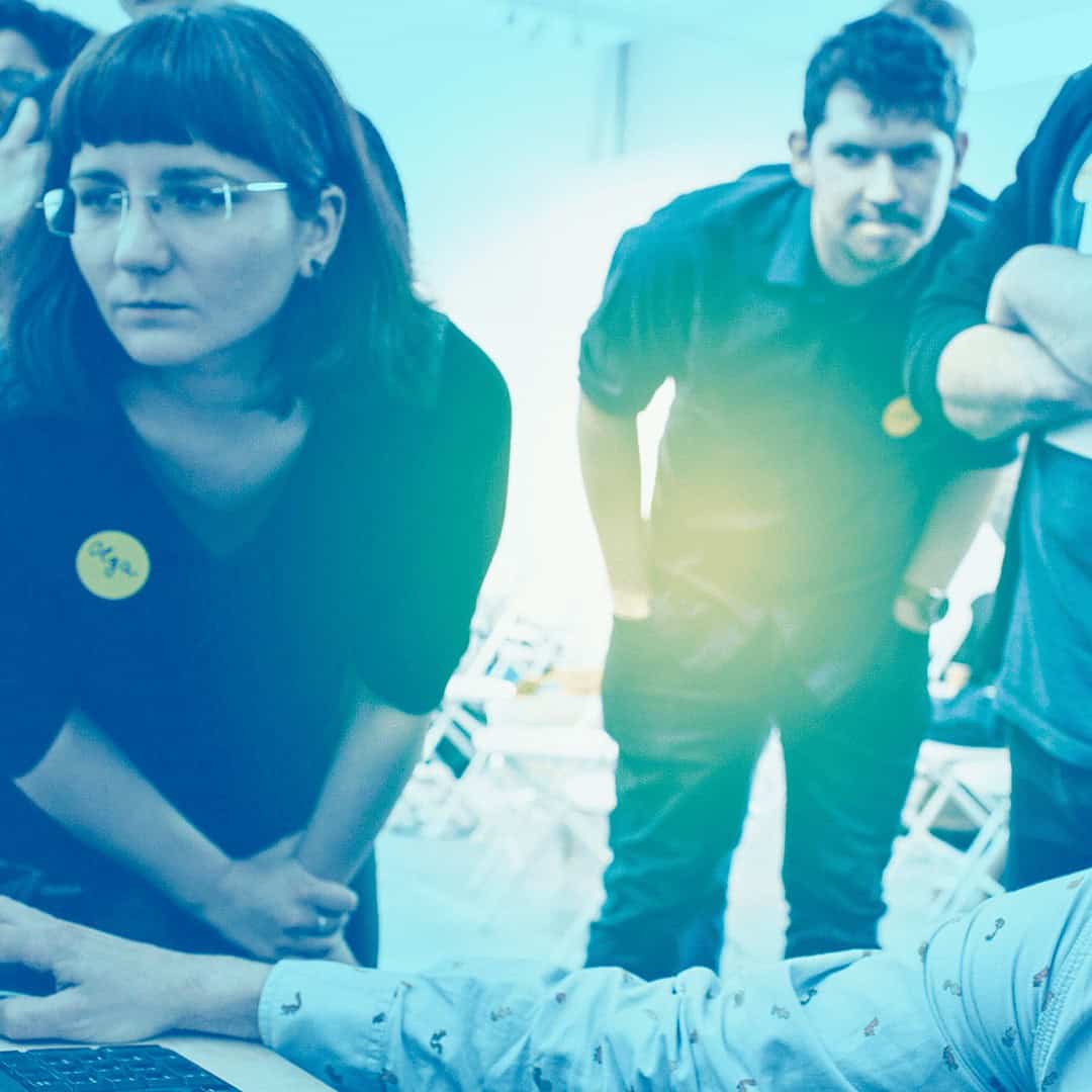 A group of students working collaboratively around a computer, with a blue tint over the image.